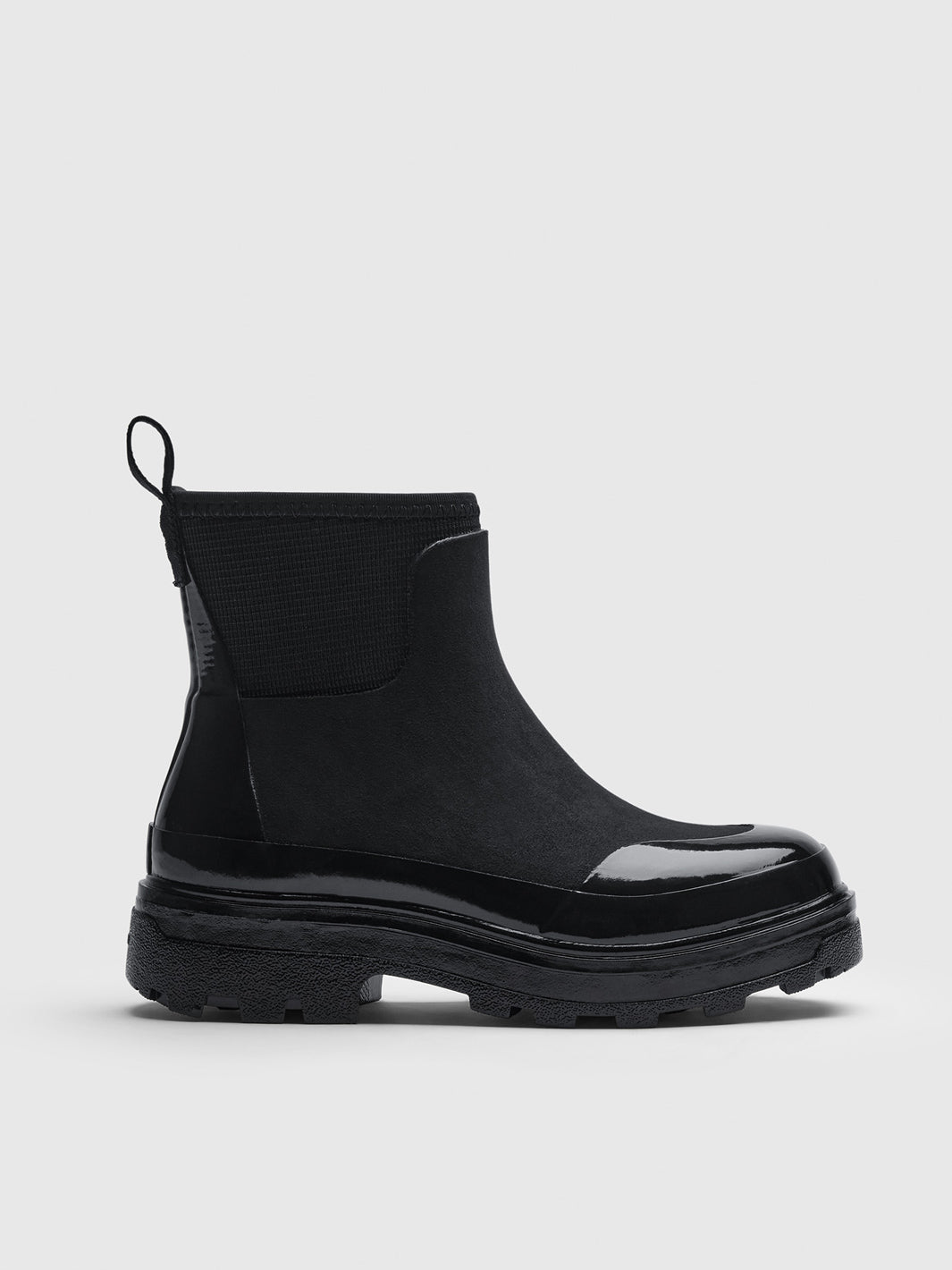 A black Chelsea-style ankle boot with a glossy patent leather toe cap and a chunky lug sole.