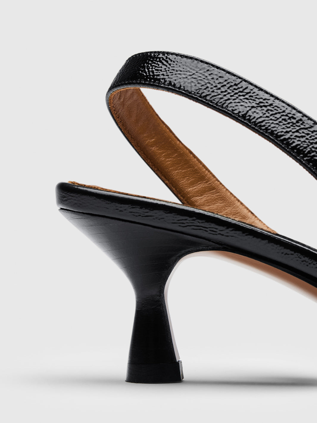 Close-up of a black slingback high heel shoe with a textured strap, a flared block heel, and a tan interior lining, shown on a light gray background.