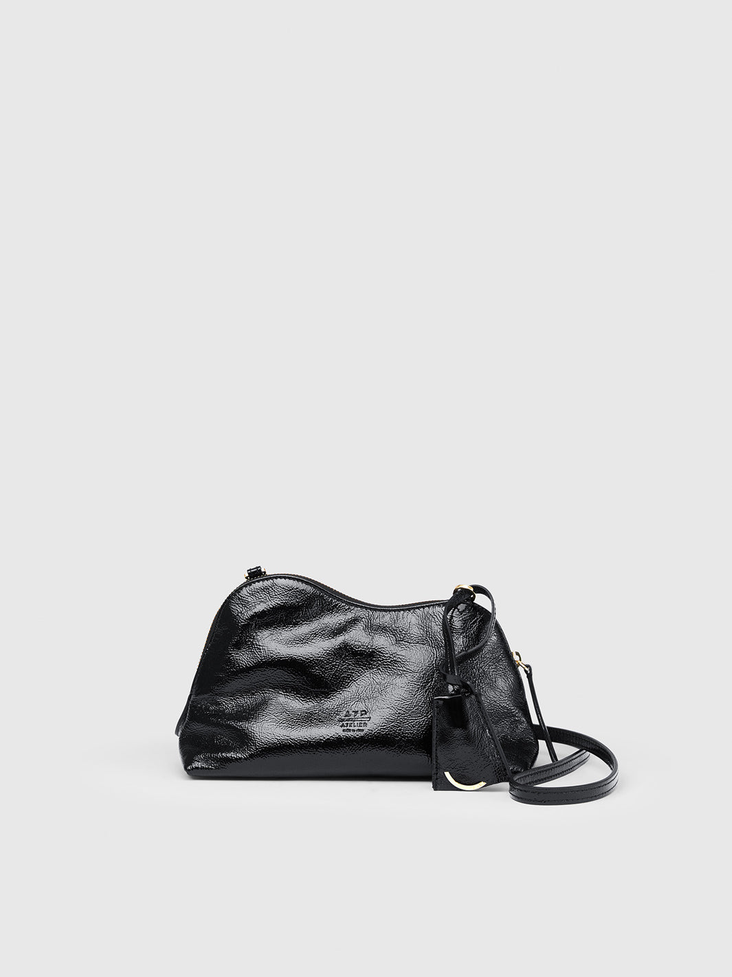 A black textured leather shoulder bag with a matching black leather tassel charm and a thin black strap, on a light gray background.